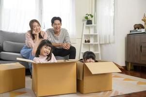 familia asiática esposo y esposa e hijos con cajas de cartón divirtiéndose el día de la mudanza, concepto de hipoteca, préstamo, propiedad y seguro. foto