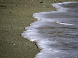 espuma de olas de mar en la orilla de la playa de arena foto
