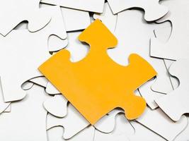 one yellow piece on pile of white jigsaw puzzles photo