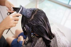 una joven asiática tiene un corte de pelo y un spa con un peluquero de belleza profesional. mujer sentada en la silla de belleza - salón de belleza mientras el peluquero le corta el pelo. foto