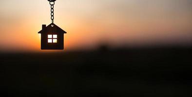 Silhouette of a house figure with a key, a pen with a keychain on the background of the sunset. They dream of a house, building, moving to a new house, mortgages, renting and buying real estate photo