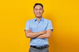 portrait of smiling young asian man in glasses holding hands together and feels optimistic isolated on yellow background. businessman and entrepreneur concept photo