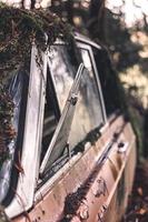 viejo coche abandonado y oxidado en un bosque cubierto de musgo foto