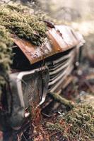 viejo coche abandonado y oxidado en un bosque cubierto de musgo foto