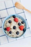 Ofsyan porridge with raspberries and blueberries in a blue bowl on a light background photo