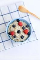 Porridge with berries for breakfast. Oatmeal in a blue plate with a wooden spoon on the table view from above photo