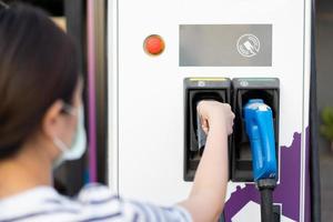 mujer joven asiática preparándose para cargar su vehículo eléctrico o auto ev en la estación de carga ev. foto