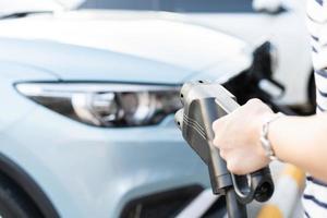 mujer joven asiática preparándose para cargar su vehículo eléctrico o auto ev en la estación de carga ev. foto