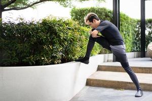 joven deportista asiático haciendo ejercicio en el parque al aire libre, antes del ejercicio estirando todo el cuerpo. foto