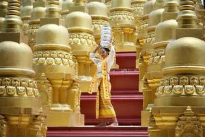 Young Asian girl in traditional Burmese costume holding bowl of rice on hand at golden pagoda in Myanmar temple. Myanmar women holding flowers with Burmese traditional dress visiting a Buddhist temple photo