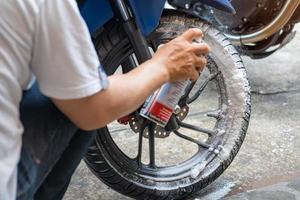 Man washing motorcycle or scooter and spraying snow foam on   Tyre wheels .Tyre restoration maintenance ,repair motorcycle concept in garage .selective focus photo