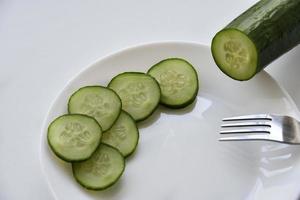 Whole and sliced cucumber on a white plate and fork photo