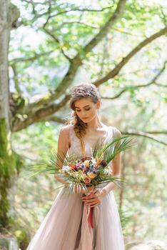Happy bride in a pink wedding dress. The girl holds a wedding bouquet in her hands. Boho style wedding ceremony in the forest. photo