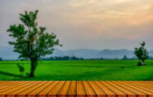 mesa de madera y desenfoque de belleza en un día de puesta de sol en un campo con cielo y montañas en el fondo. foto