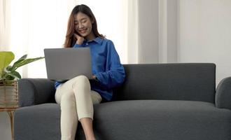 Young business freelance Asian woman working on laptop checking social media while lying on the sofa when relax in living room at home. photo