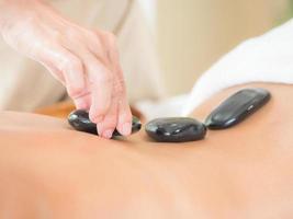 An expert masseuse at a spa salon puts hot stone on the back of an Asian woman to relieve tension from work photo