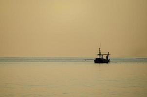 Silhouette of fishermen collecting fishing gear on a small fishing boat. The sea in the sunrise. Golden hour. photo