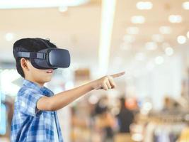 Boy wearing virtual reality glasses in modern interior design studio and trying to touch dots network and earth map or something appear in VR with exciting.Flares effect, blurred background concept. photo