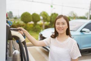 mujer hermosa joven asiática preparándose para cargar un vehículo eléctrico o ev en la estación de carga ev. foto