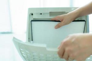 hermosa joven asiática sosteniendo un filtro purificador de aire de carbono hepa en la sala de estar, la mujer prepara un filtro purificador de aire para reemplazar el anterior. concepto de salud y buen estilo de vida. foto