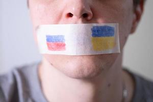 Scotch-taped mouth with the flag of Russia and Ukraine, trying to say. photo