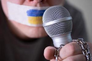 cinta sobre su boca con la bandera de ucrania, tratando de hablar en un micrófono. foto