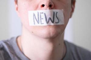 A man gags his mouth with duct tape that reads the news. photo