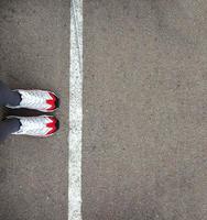 Feet in sneakers stand near the dividing line on the asphalt. Bounding line, social distance, waiting in line. The border, stand in line for a start. Copy space photo