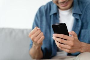 hombre emocionado feliz mirando el teléfono móvil, hombre recibiendo buenas noticias usando el teléfono inteligente en casa. foto