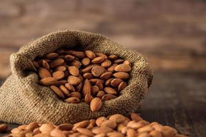 almendras en bolsa de saco sobre mesa de madera.materia prima orgánica foto