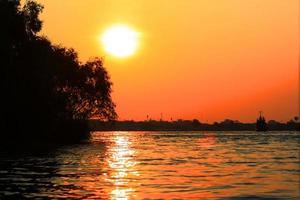 hermosa puesta de sol en el río con carguero y barco en Tailandia foto