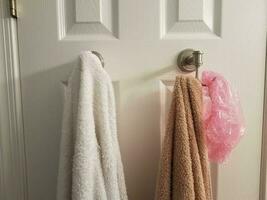 white and brown towel on hook on bathroom door with pink showercap photo