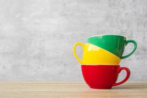 pila de coloridas tazas de café en el fondo de la pared en el café. taza de cerámica de color verde, amarillo y rojo en la mesa en casa. concepto del día internacional del café foto