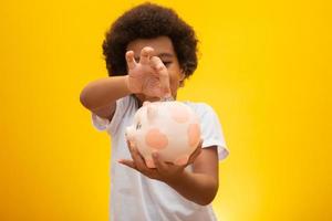 Black boy collecting money to piggy bank. Little boy putting money into piggy bank for future savings, multicultural together education concept. photo