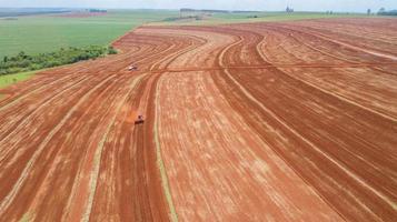 Aerial view of tractor with mounted seeder performing direct seeding of crops on plowed agricultural field. Farmer is using farming machinery for planting process, Brazilian farm. photo