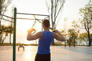 entrenamiento masculino en forma en el verano, ejercicios con correas de suspensión al aire libre foto