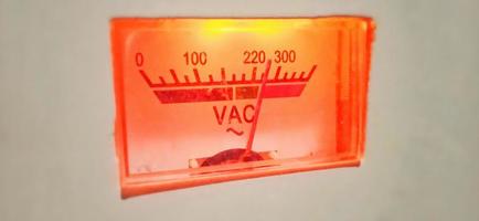 An isolated red-orange old volt ampere meter electrical equipment display under dim condition. photo