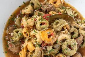 bowl of tortellini pasta soup with herbs flat lay photo