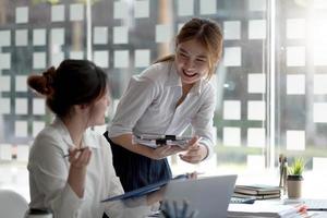 dos jóvenes empresarias trabajadoras que trabajan juntas en sus computadoras portátiles leen pantallas con caras sonrientes en ángulos altos. foto