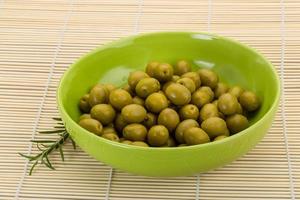 Green olives in a bowl on wooden background photo