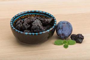 Dried plums in a bowl on wooden background photo