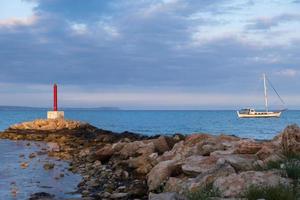 Lighthouse and Sailboat bathed in afternoon light in Potamos Liopetri fishing village, Mediterranean, Cyprus photo