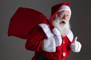 Santa Claus in eyeglasses is looking at camera and smiling, on gray background photo