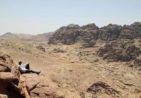 joven en la cima de un pico con vistas a un valle en el accidentado paisaje de petra, jordania foto