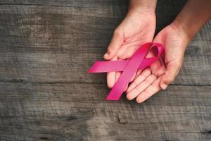 concept healthcare and medicine. hand holding pink ribbon on wood. breast cancer awareness. sign of hope photo