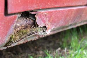 Rusty driver's door sills. Corrosion of the body of a red old car after winter. Influence of reagents in winter on an unprotected vehicle body. Damage to the left side, rotten threshold on the bottom. photo
