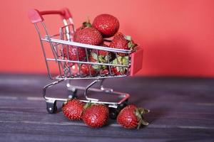 Small cart full of fresh ripe strawberries against a red background. photo