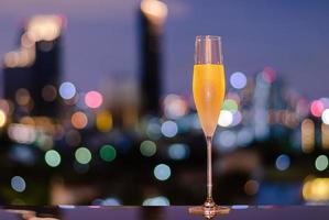 A glass with vapour of cold Champagne on table with colorful city bokeh lights background. photo