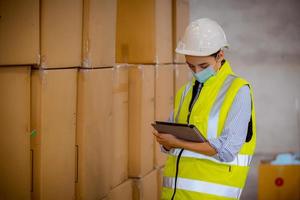 Factory engineer under inspection and checking quality production process on face mask manufacture  station by  wearing casual uniform and safety helmet in factory plantation. photo