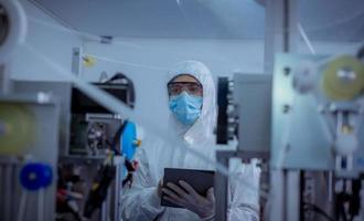 Technician worker wearing protective suite , glove are inspect machine with check  face mask manufacturing process to safe and against from virus photo